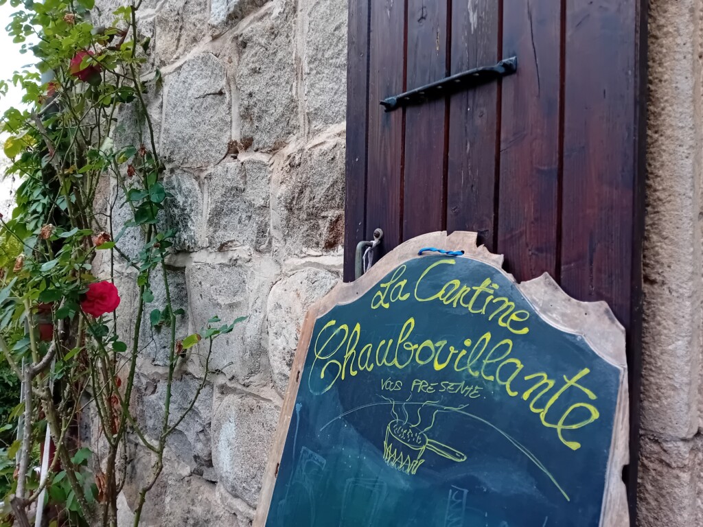 "La Cantine Chaubouillante vous présente" : haut d'un grand tableau à craie reposant sur un mur en pierres contre lequel grimpe un rosier