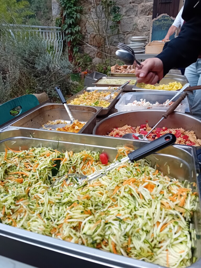 Buffet en libre service : une table recouverte de plusieurs plats aux contenus colorés, une main tenant ses couverts